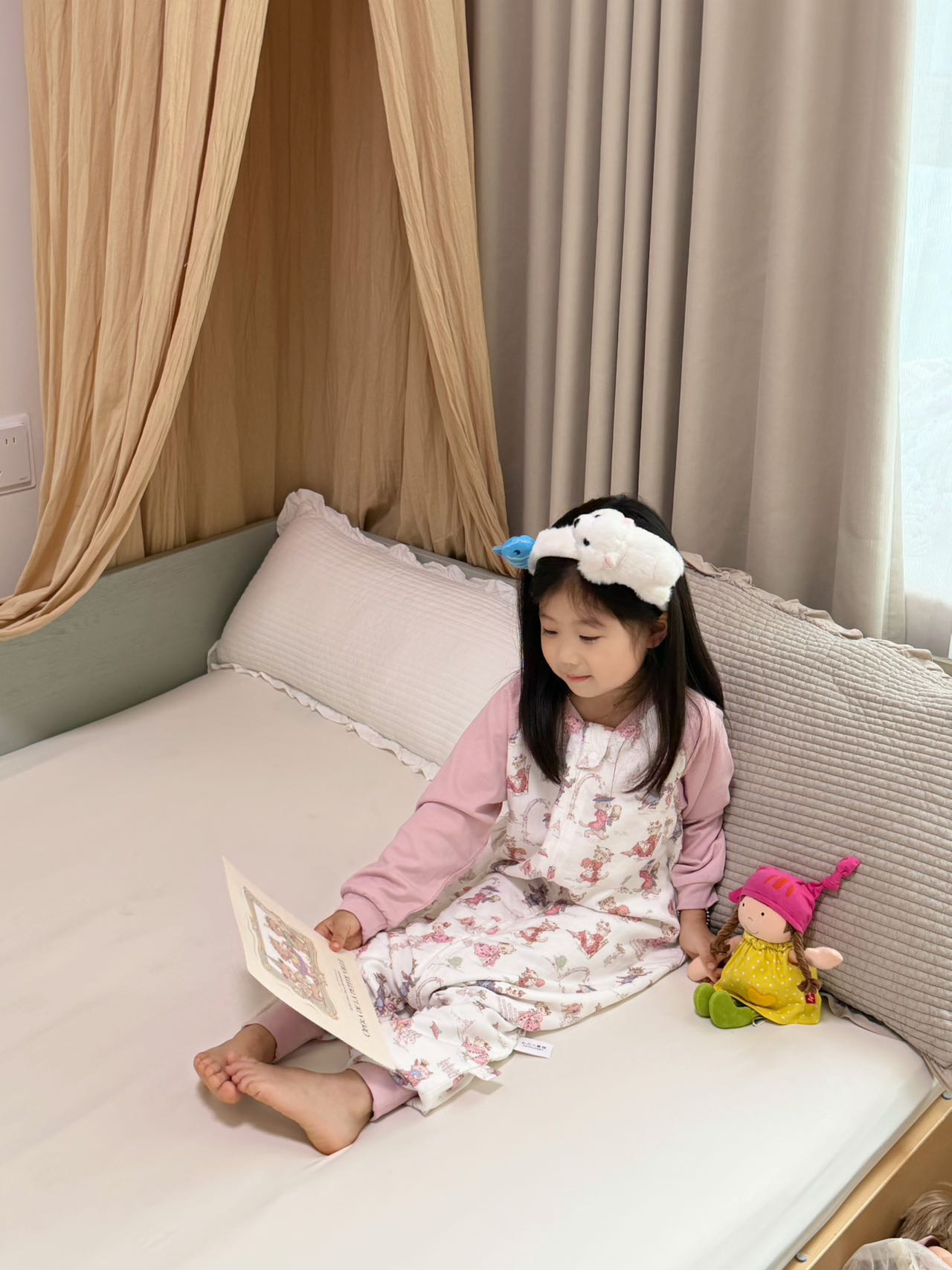 孩子穿着粉色睡袋坐在床上读画册